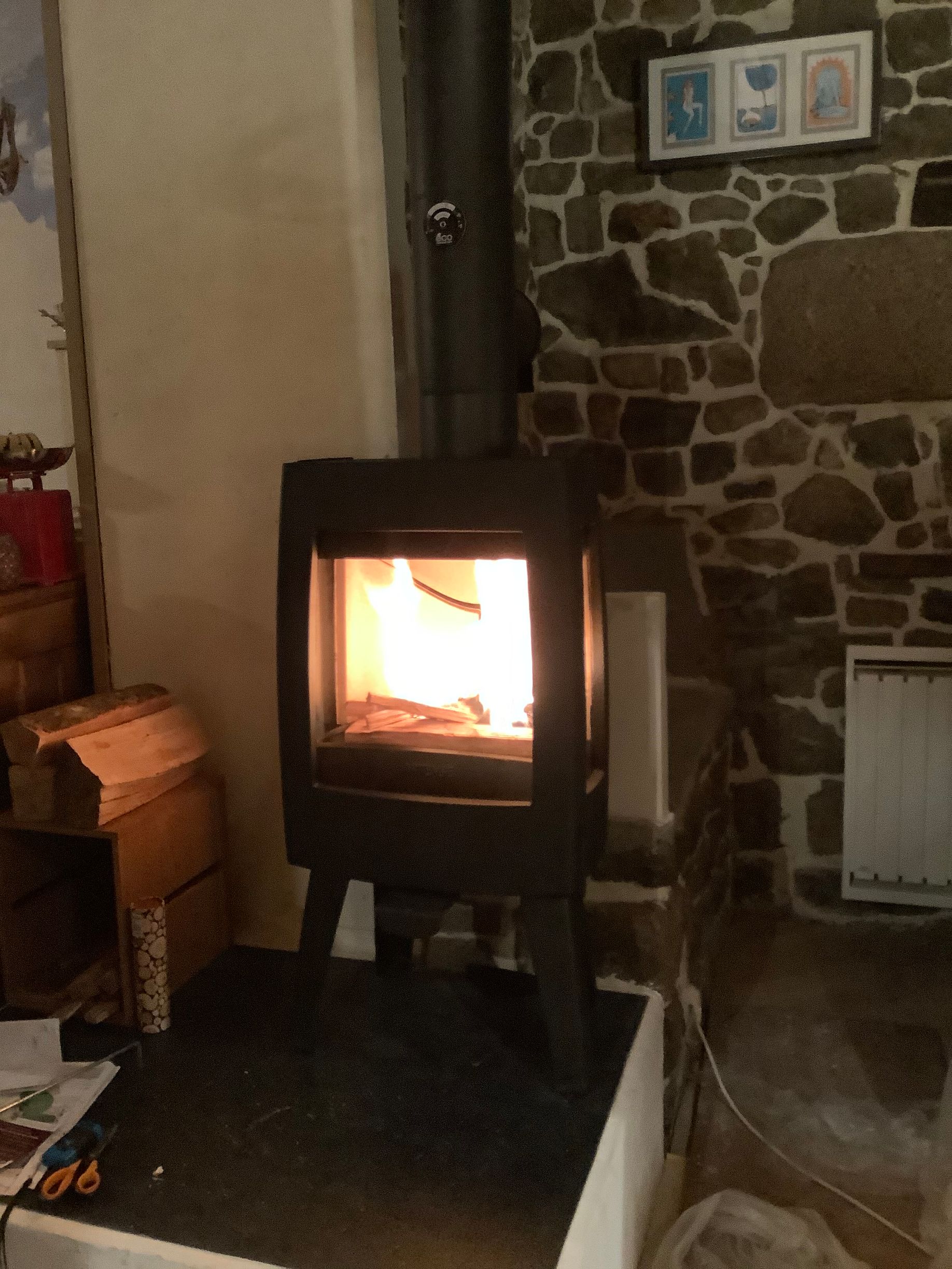 Un poêle à bois moderne, aux flammes crépitantes, est installé sur un foyer en pierre.