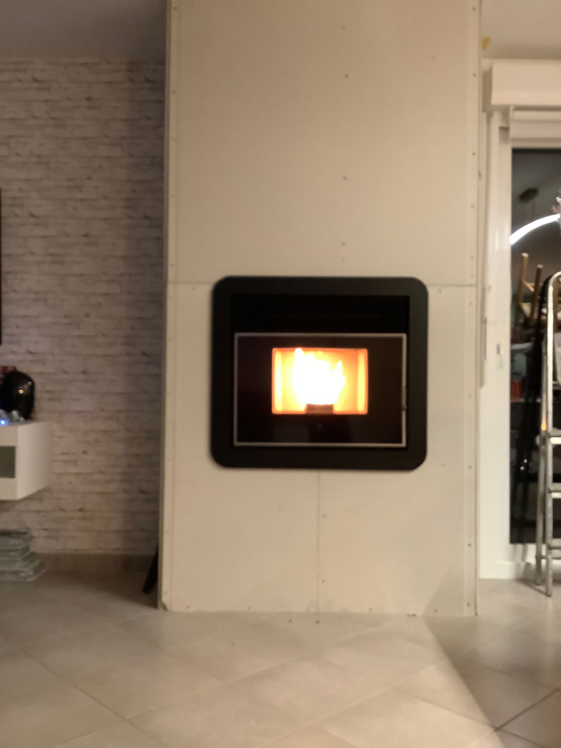 Un poêle à granulés moderne de forme carrée, à la flamme orange vif, encastré dans un mur clair et uni.