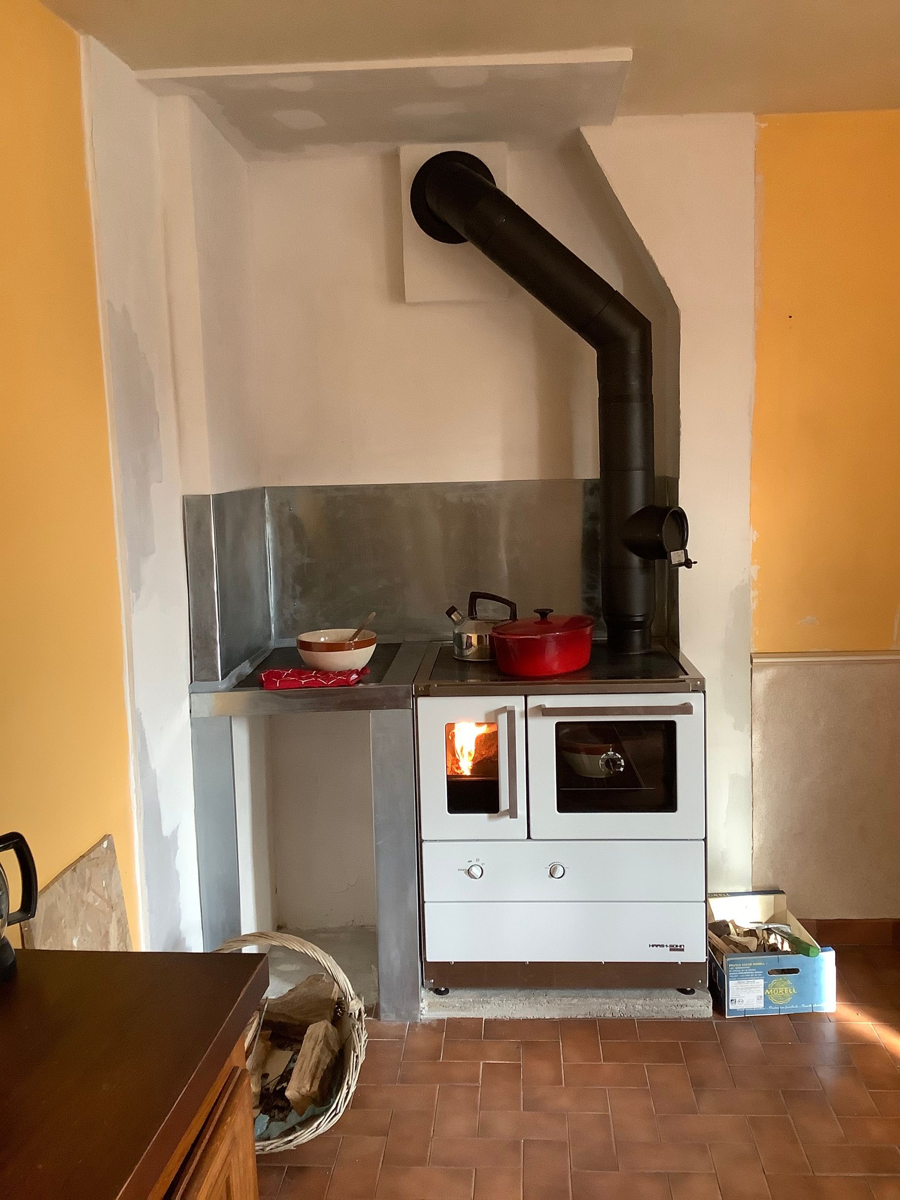 Un poêle à bois avec un feu allumé, une crédence en métal et un conduit de cheminée incliné.