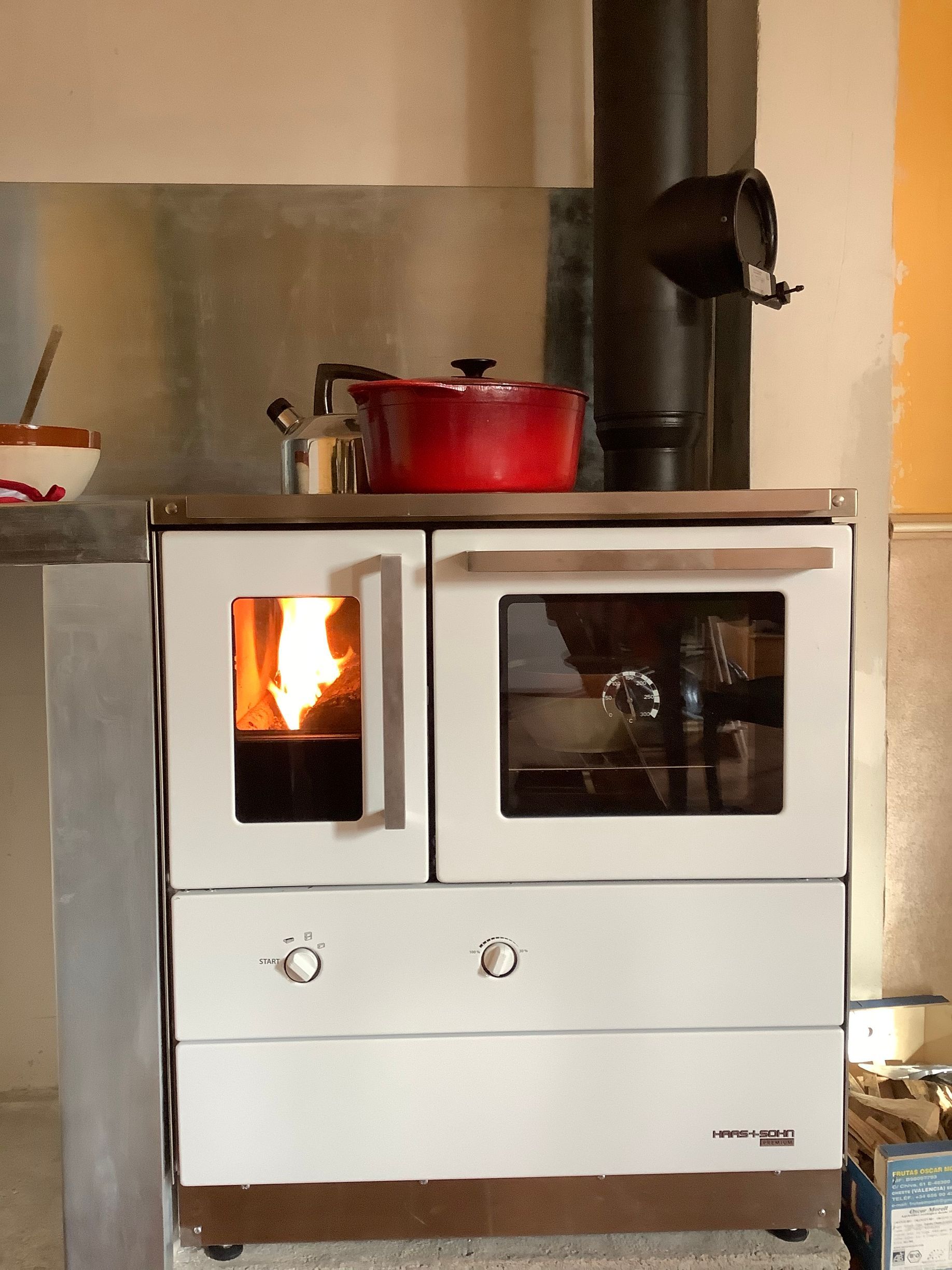 Un poêle à bois blanc, avec un feu visible et un tuyau de cheminée noir.