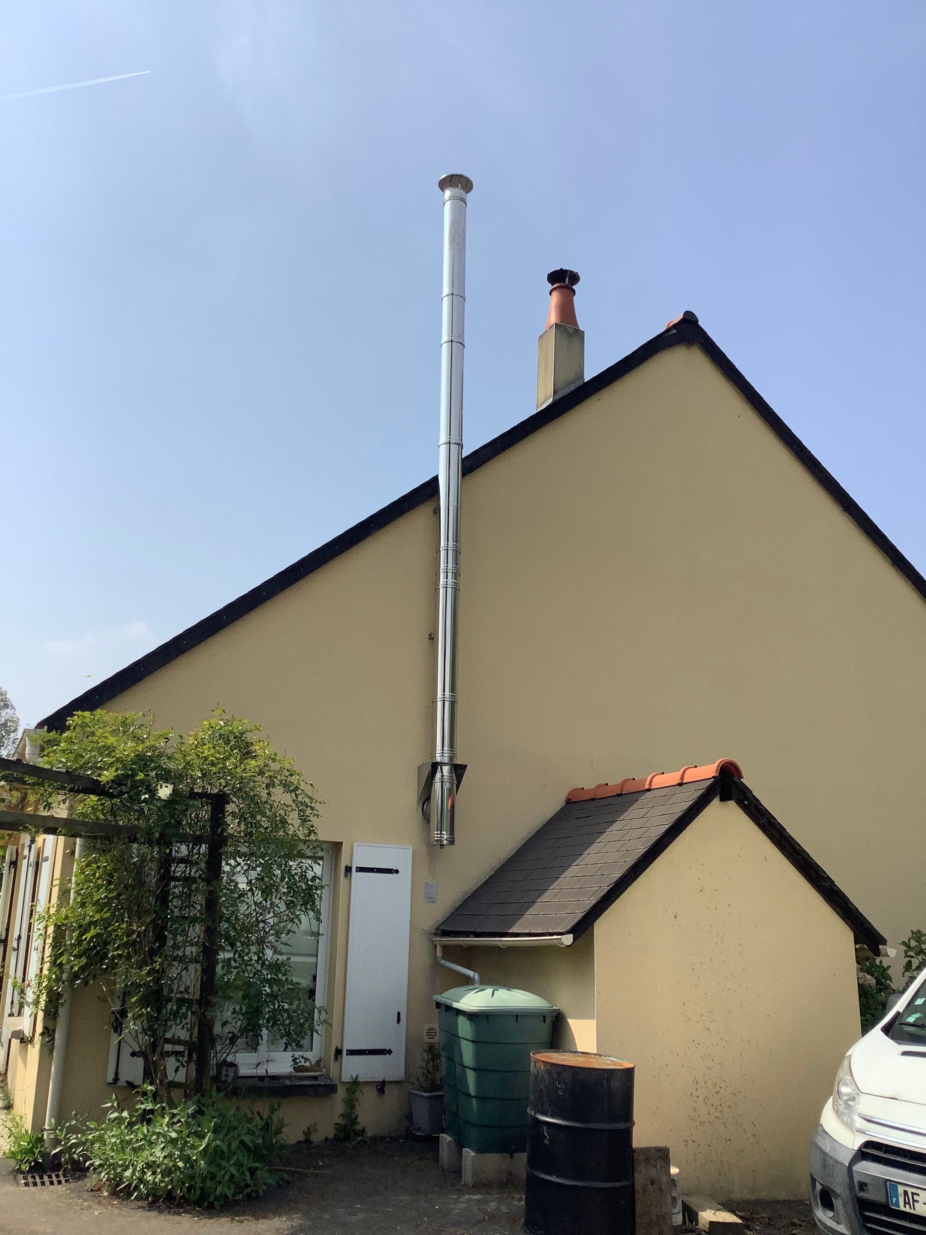 Un conduit de cheminée en métal argenté, de grande hauteur, est installé contre le mur extérieur d'une maison.