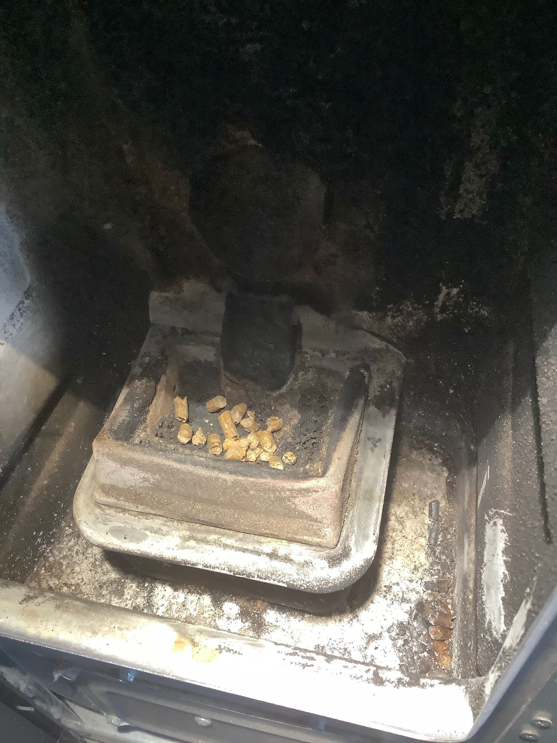 Intérieur d'un poêle à granulés, montrant le creuset métallique contenant un petit tas de granulés de bois non brûlés.