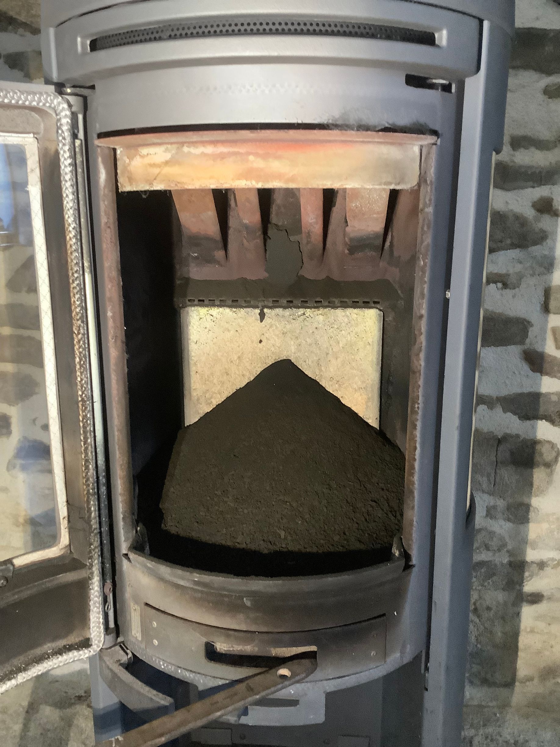 Un poêle à bois ouvert avec un gros monticule conique de cendres noires au centre du foyer.