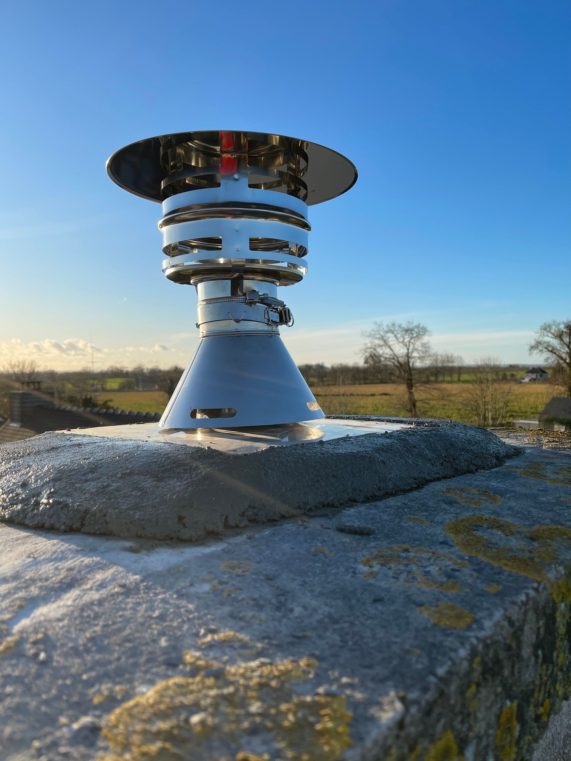 Un chapeau de cheminée en métal argenté installé sur une cheminée en pierre.