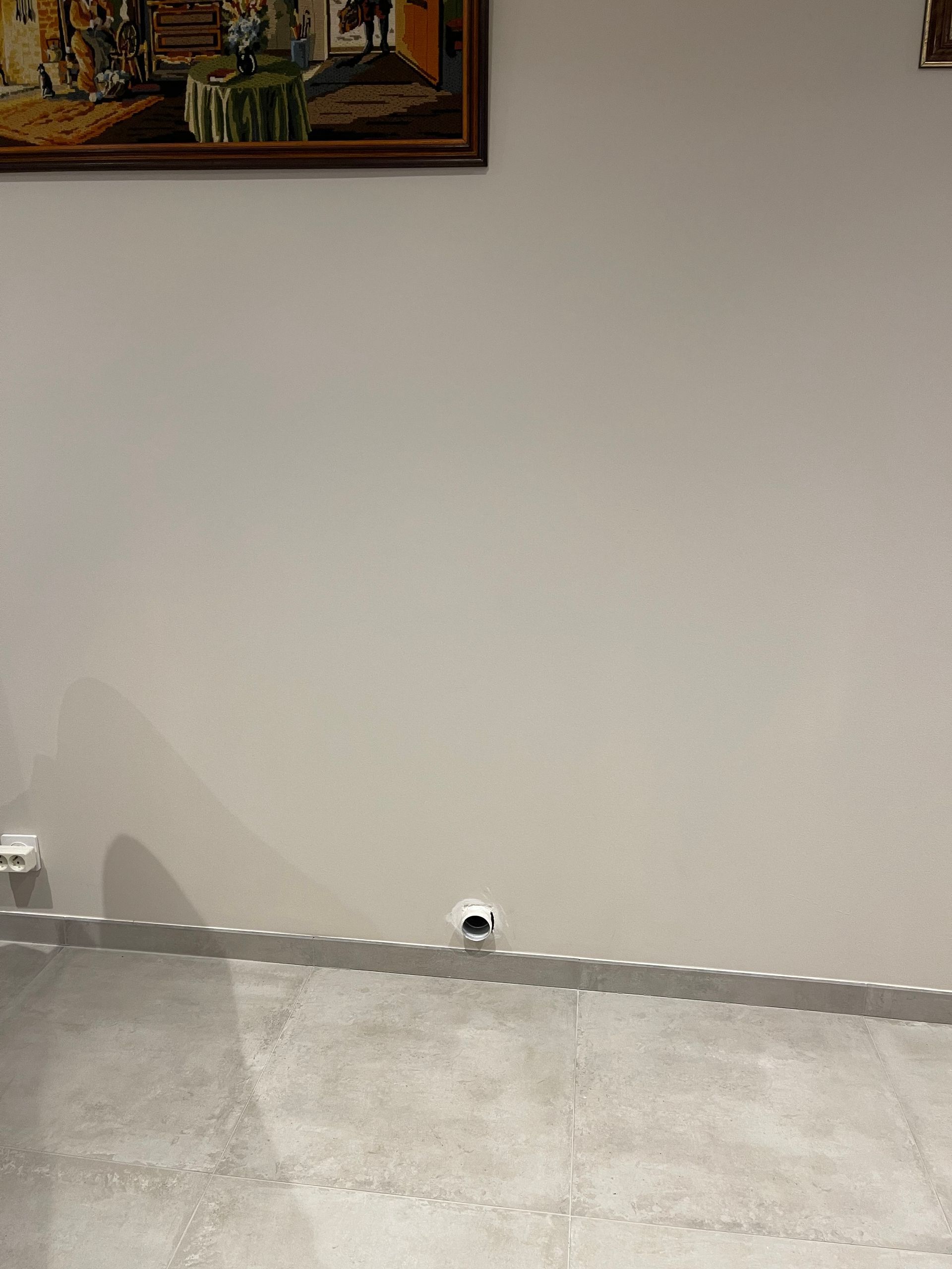 Un mur gris clair avec une petite prise circulaire blanche près du sol.