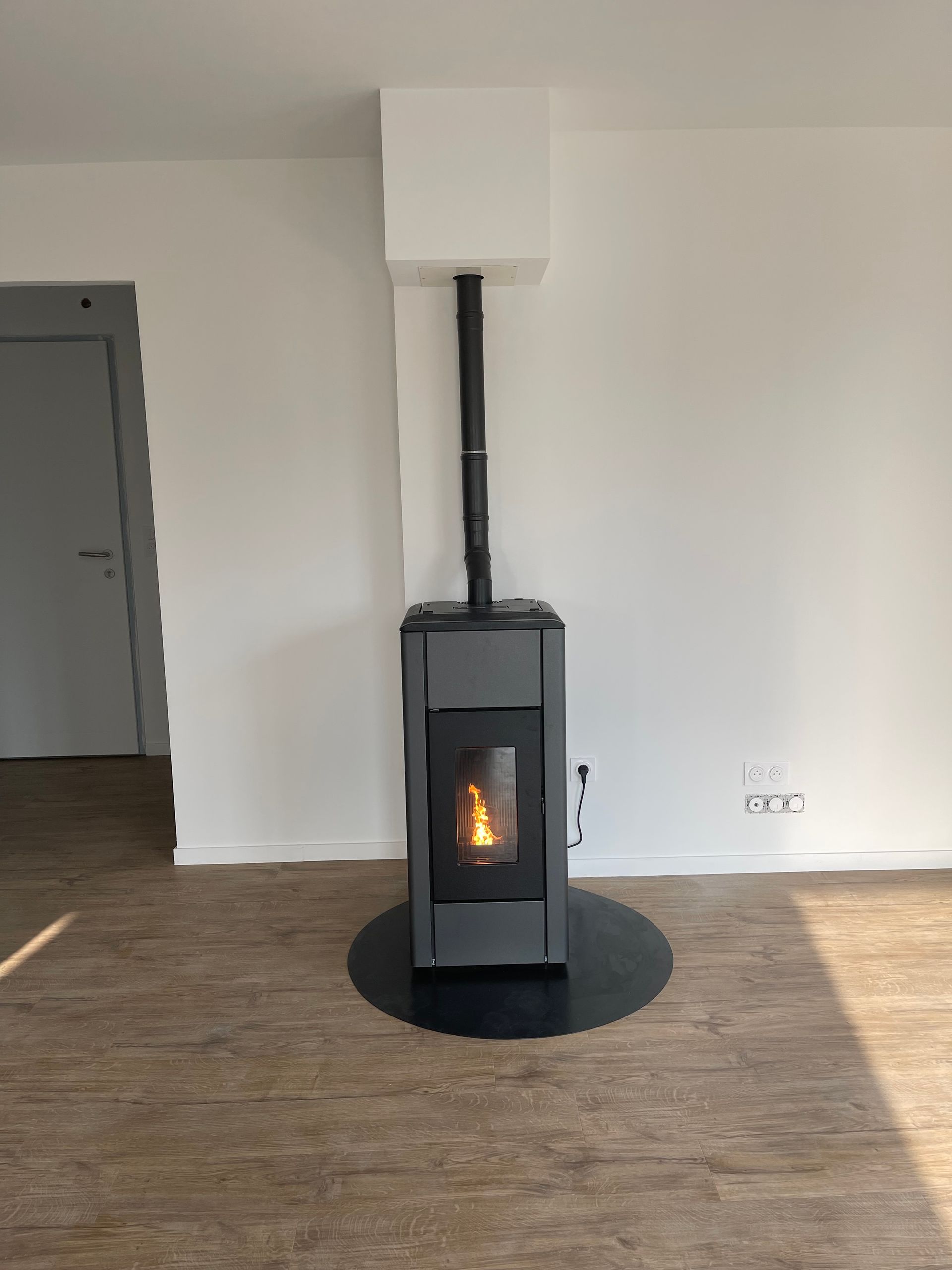 Un poêle à granulés allumé repose sur un tapis de sol noir rond.