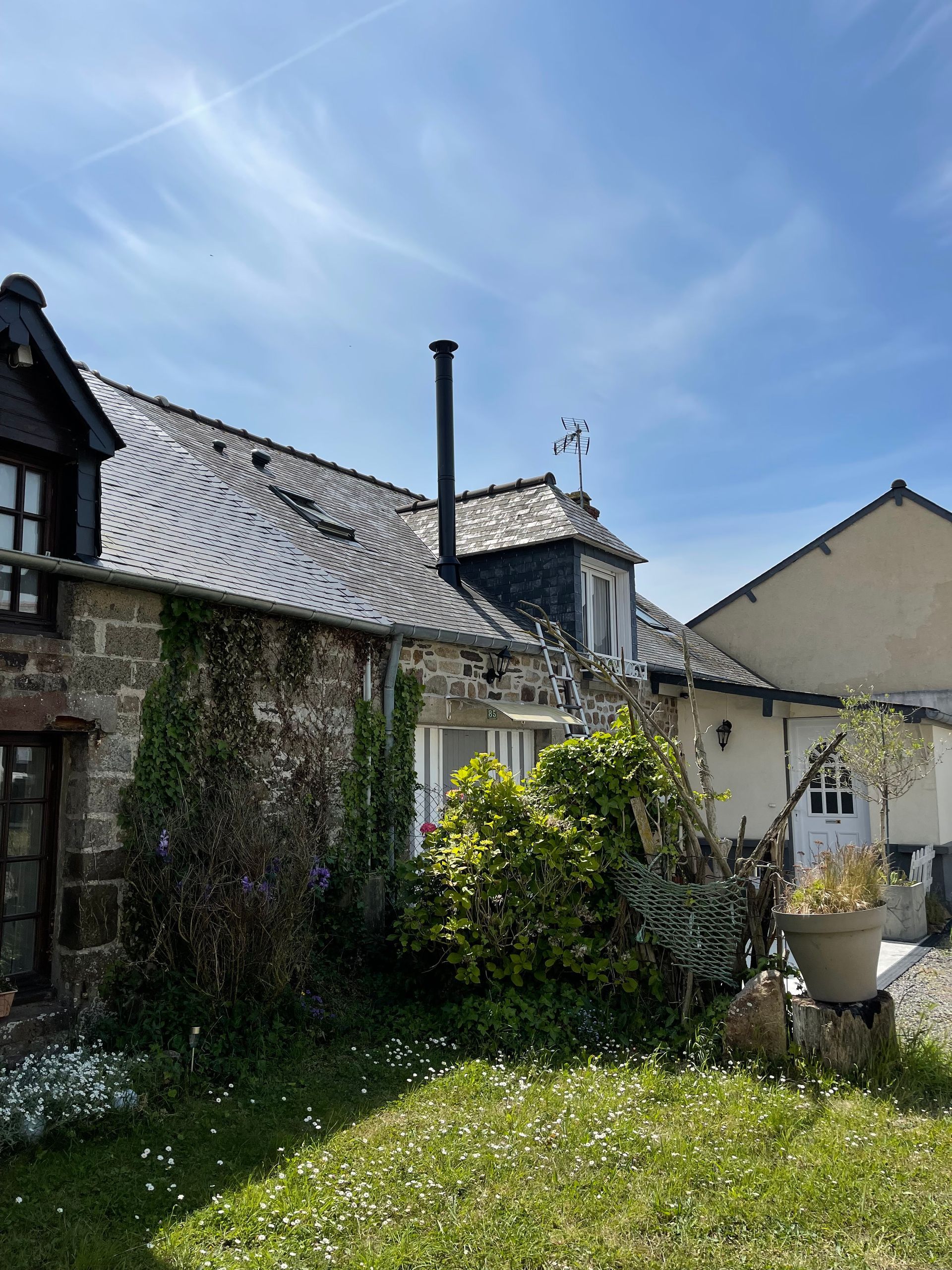 Un cottage rustique en pierre avec un toit en ardoise, une haute cheminée.