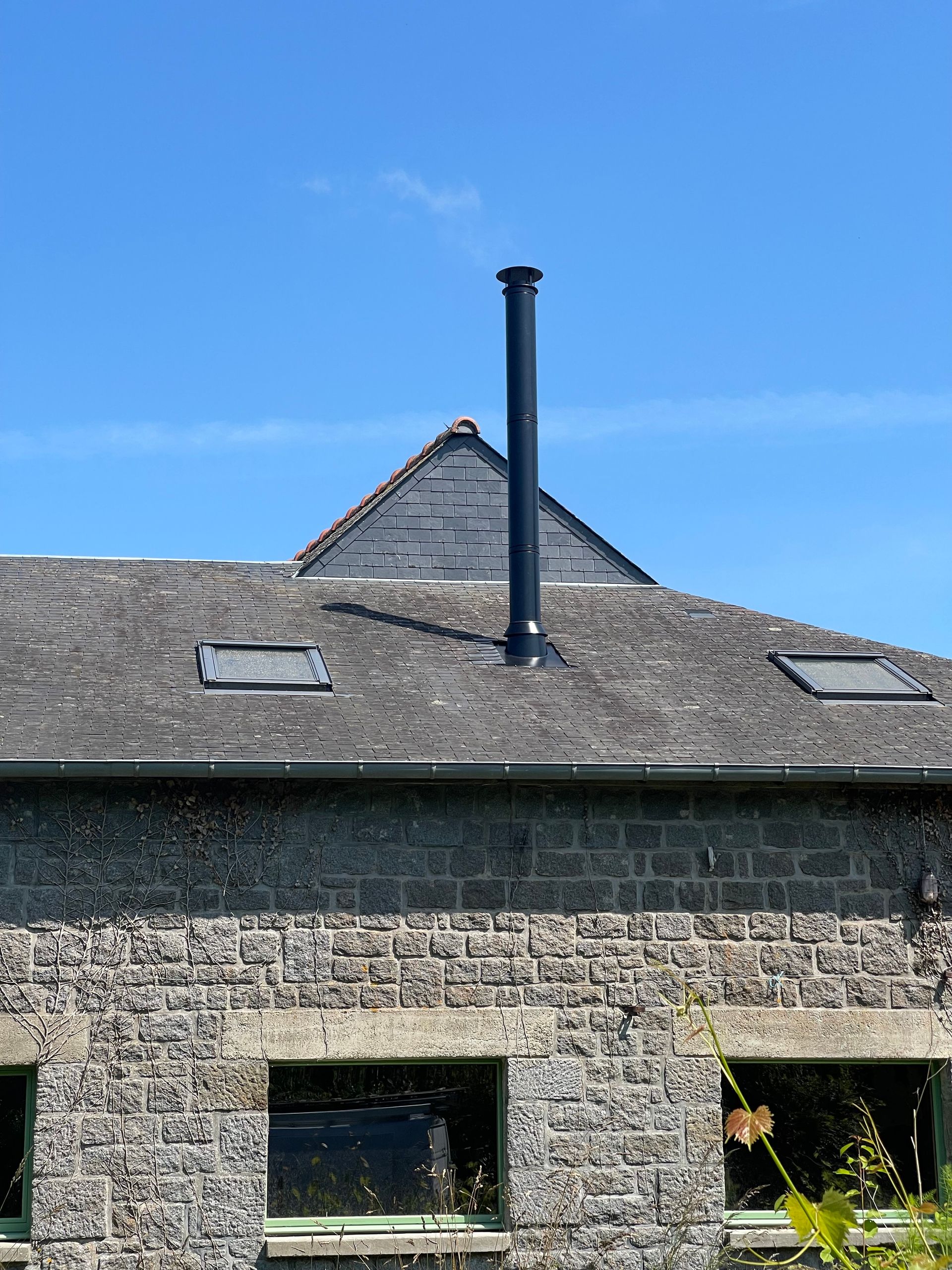 Une haute cheminée noire se dresse sur un toit d'ardoise grise texturée.