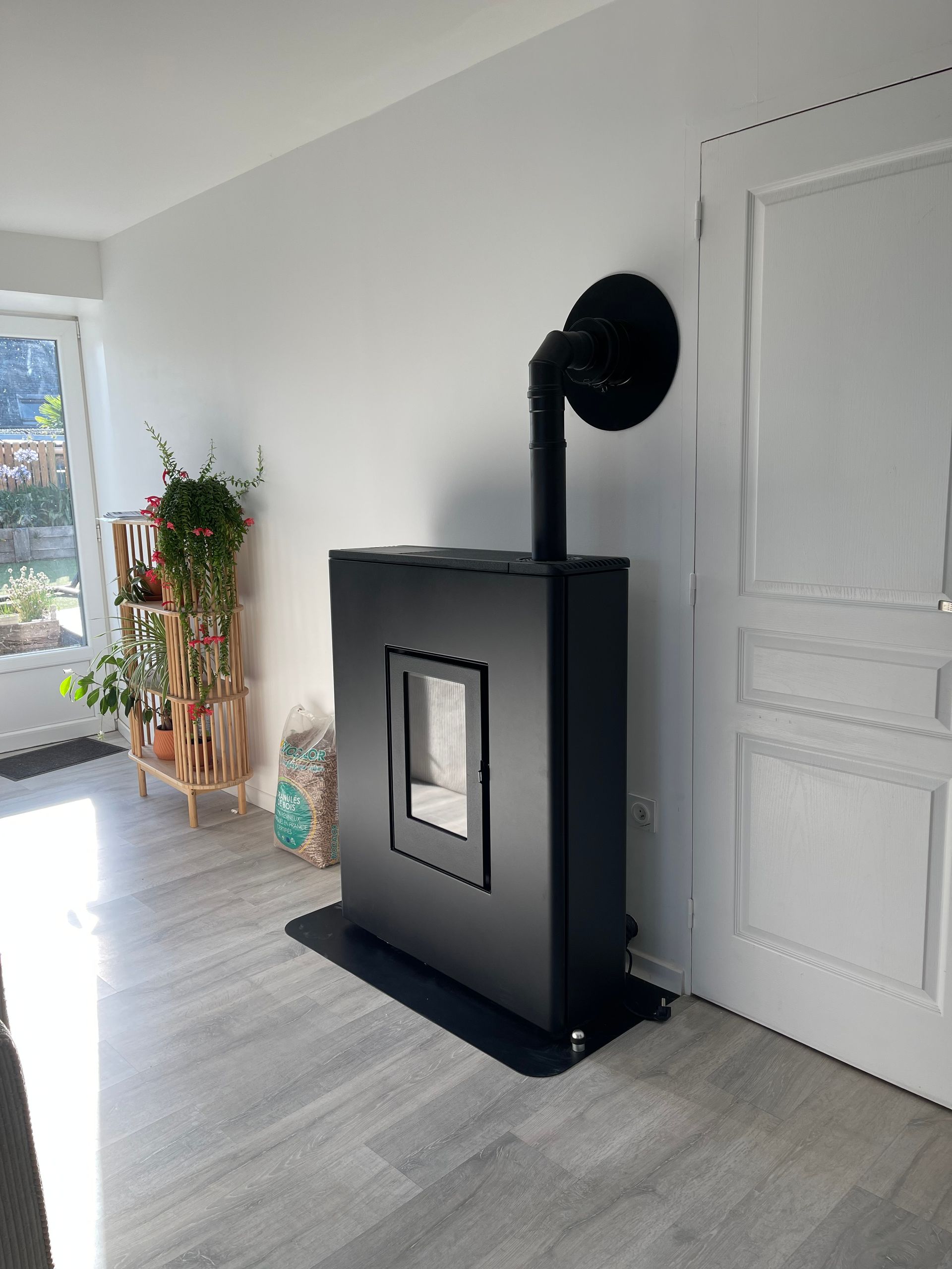 Un poêle à granulés noir est posé sur un tapis de sol contre un mur blanc.