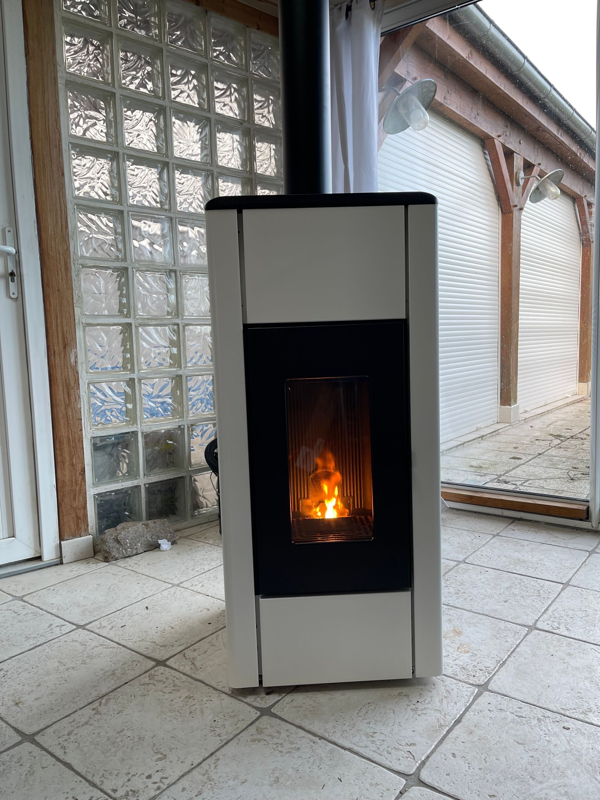 Un poêle à granulés vertical blanc, avec un panneau avant noir et des flammes visibles.