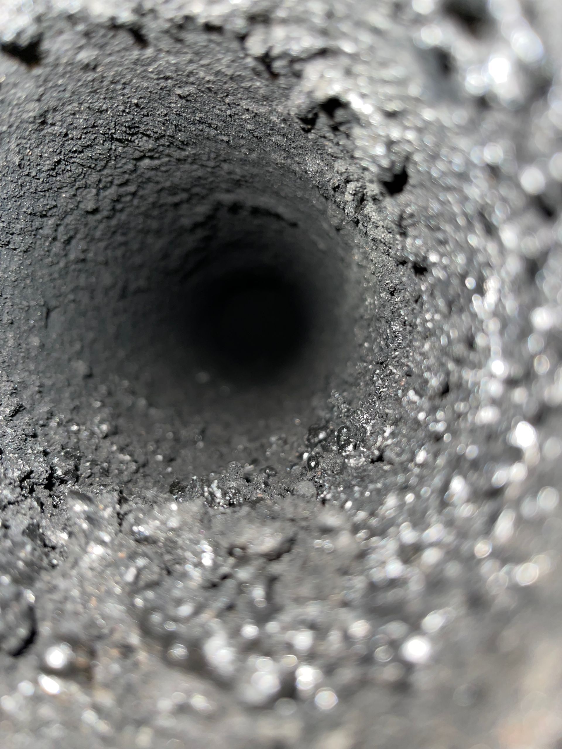 Gros plan sur l'intérieur d'un tuyau cylindrique sombre, tapissé d'une épaisse couche de suie ou de résidus gris foncé, rugueux et épais.