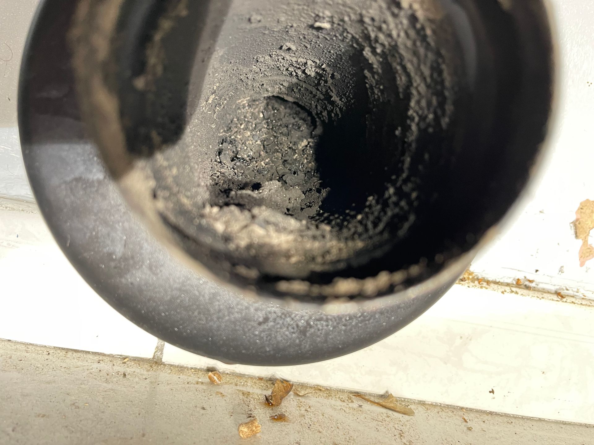 Gros plan à l'intérieur d'un tuyau montrant une accumulation importante de peluches et de débris sombres et granuleux.