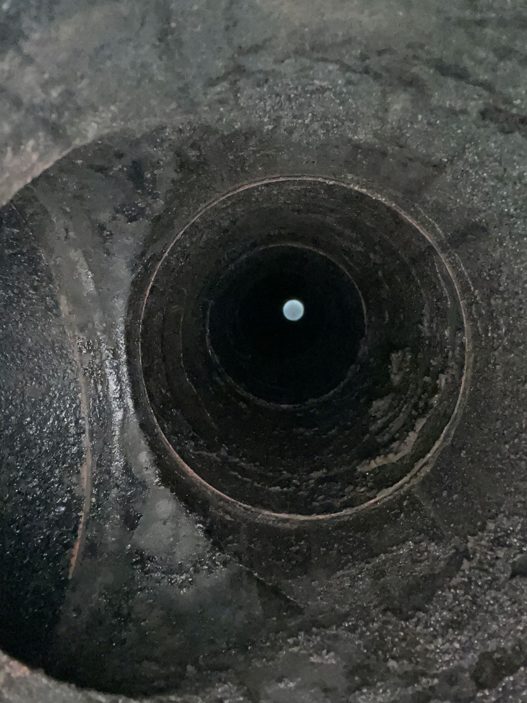 Vue d'un tunnel sombre et circulaire montrant d'importantes accumulations de suie sur les parois intérieures.