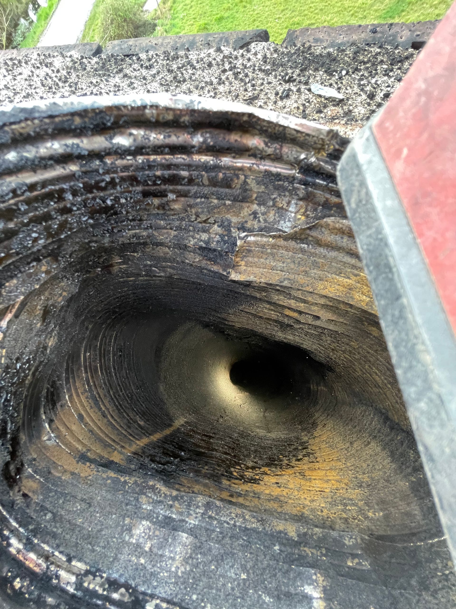 Vue de dessus d'un conduit de cheminée circulaire, sombre et recouvert de suie, montrant d'épaisses couches concentriques d'accumulation de créosote.