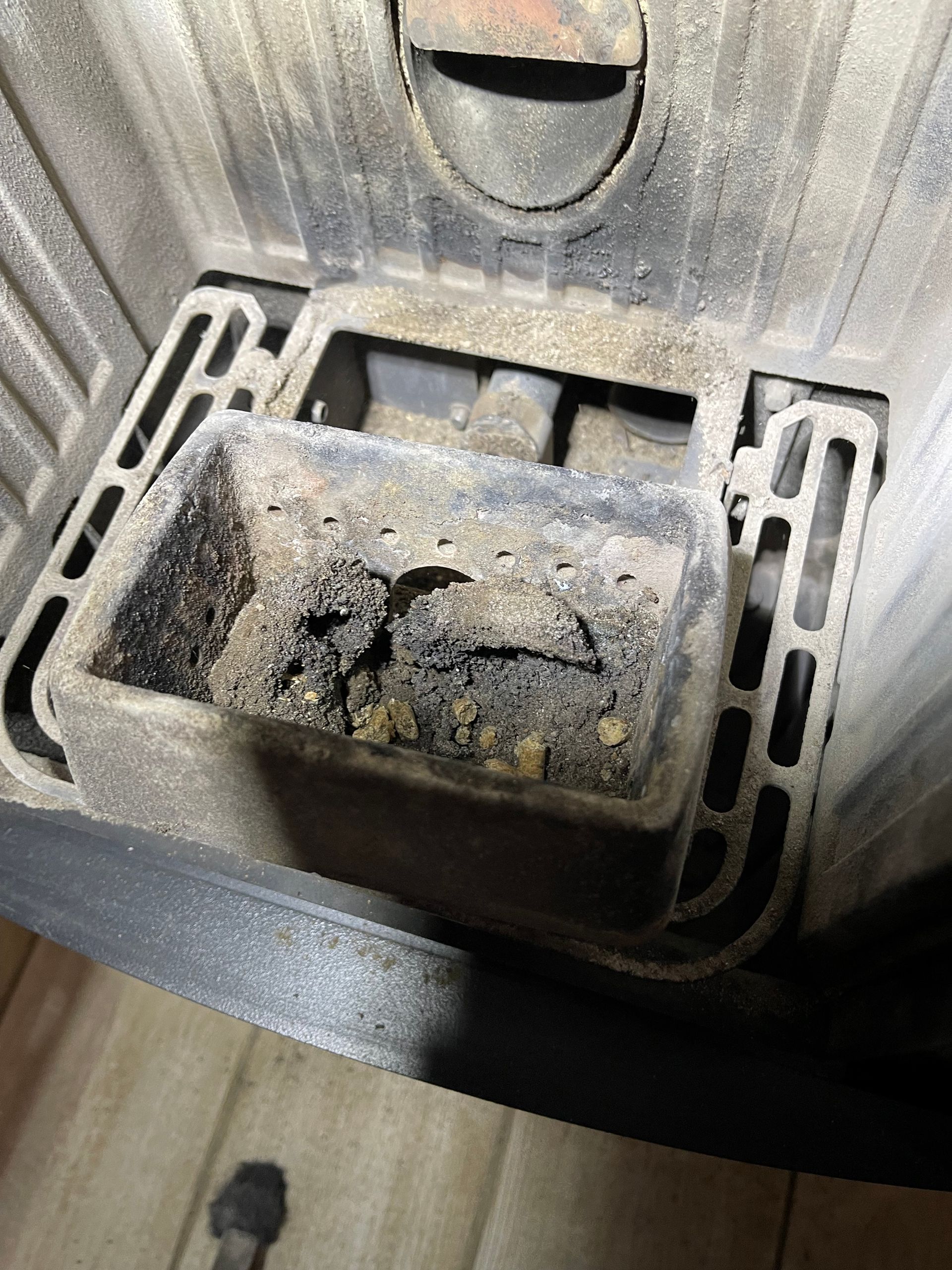 Le brûleur en fonte d'un poêle à granulés contenant des cendres et des granulés non brûlés.