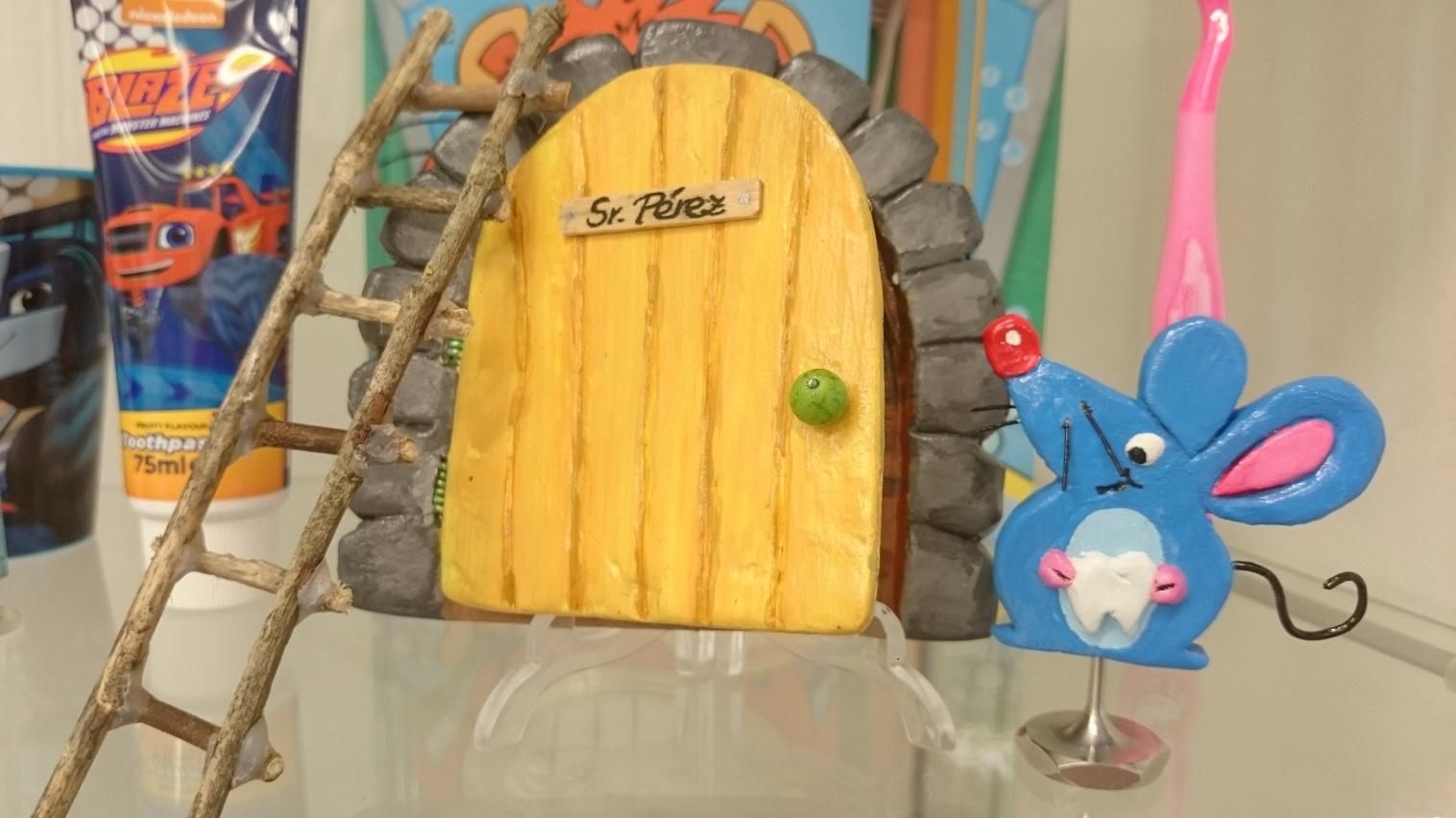 Escena de juguetes colorida con una puerta amarilla con marco de piedra y una figurita de ratón azul sobre una mesa.