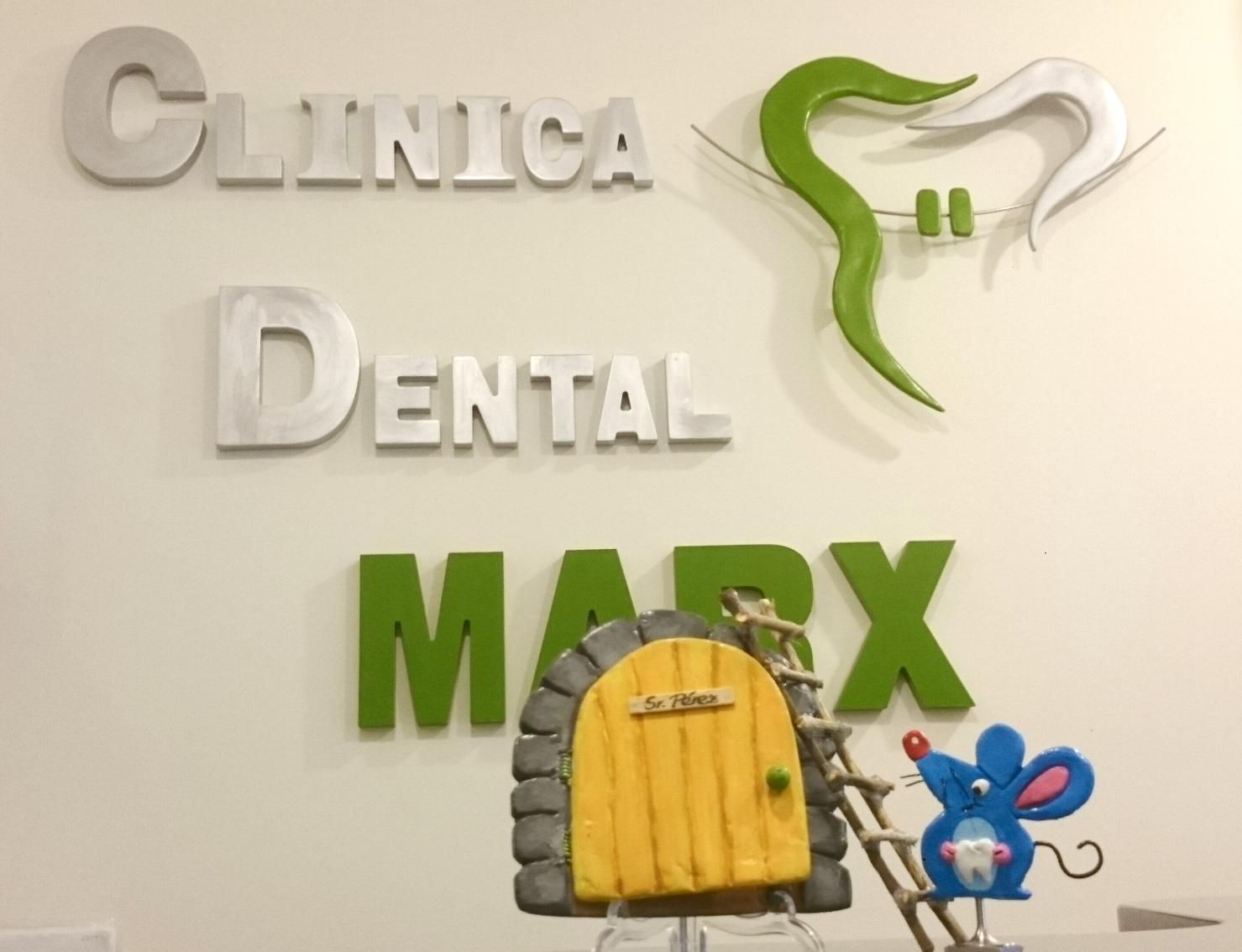 Letrero de la Clínica Dental MAX con el logotipo de un diente verde en una pared blanca, además de una pequeña puerta
