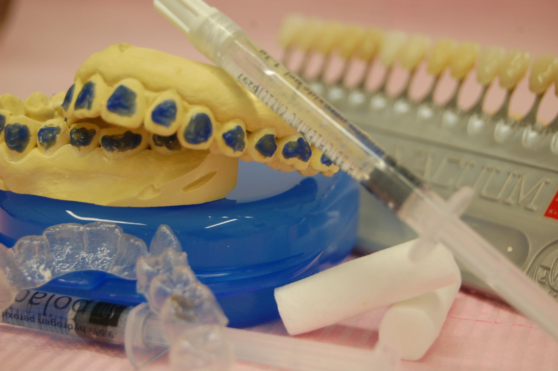 Prótesis dentales con cepillo de dientes, pasta de dientes y herramientas de limpieza dental sobre una superficie rosa.