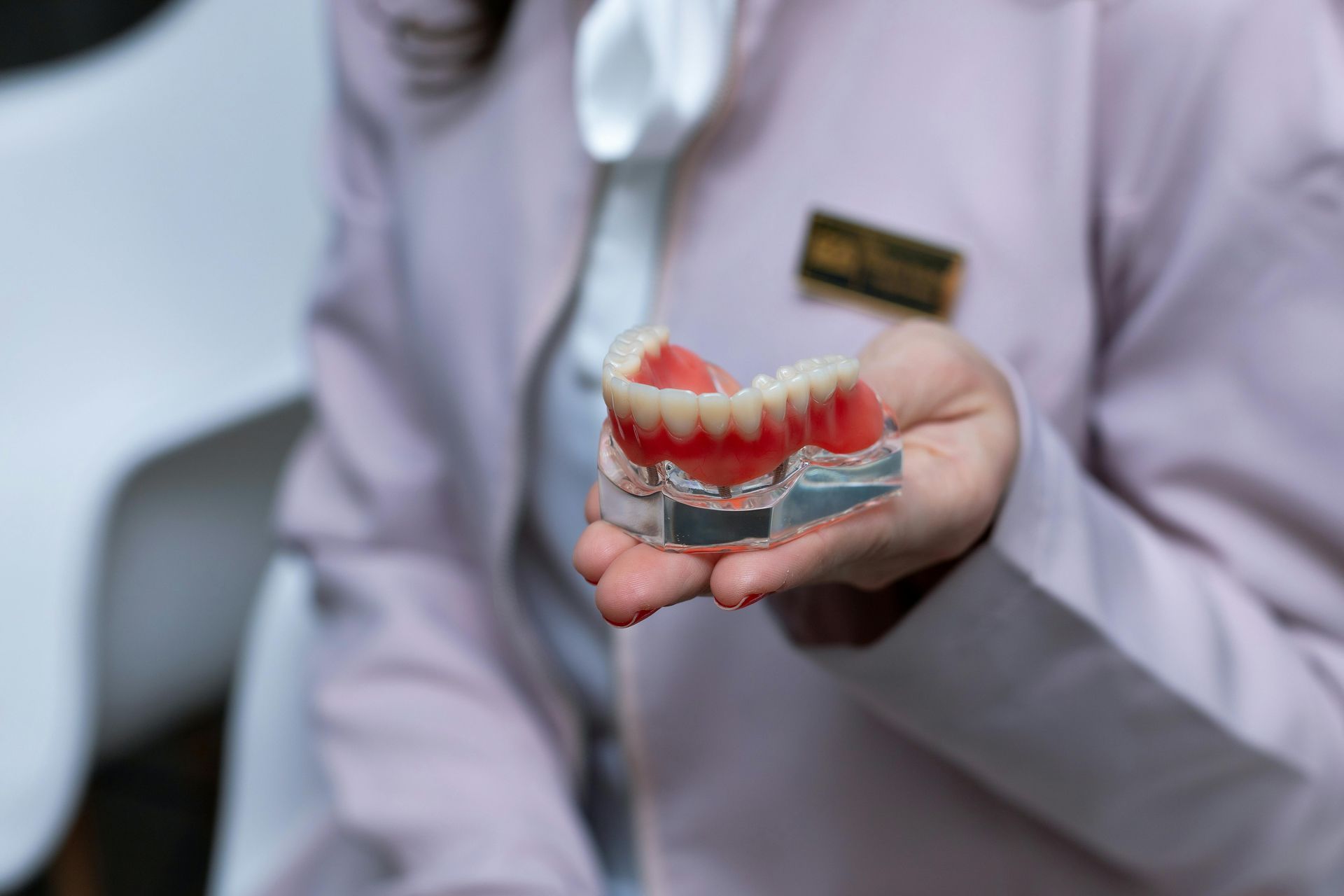 Dentista sosteniendo una dentadura postiza rosa en un entorno clínico.