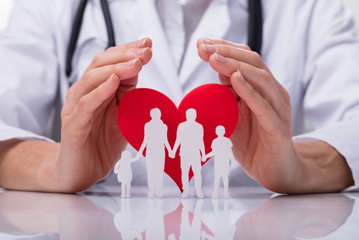Un médico sostiene un corazón rojo con una familia recortada en él.