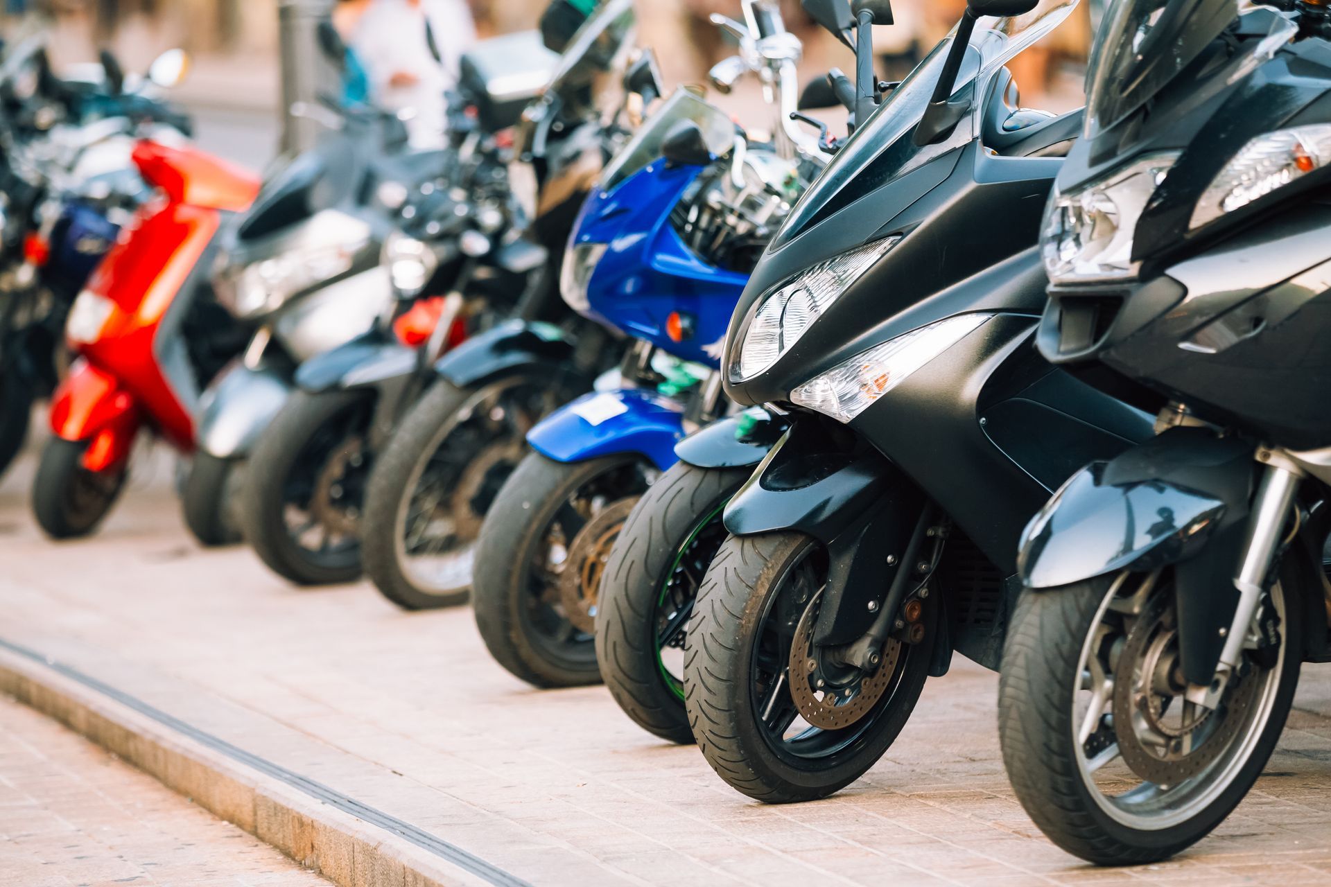Une rangée de scooters et de motos garés en ville, sur un trottoir.