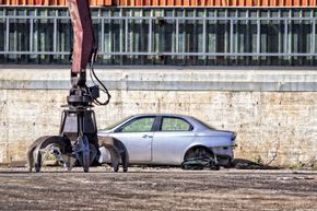 Un grappin à ferraille prêt à écraser une voiture argentée dans une casse.