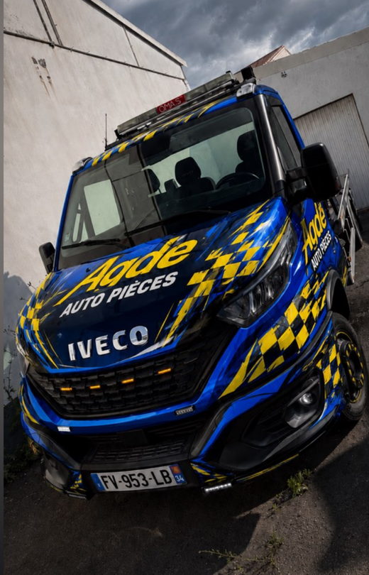 Camion de dépannage Iveco bleu et jaune mentionnant le nom de l'entreprise Agde Auto Pièces.