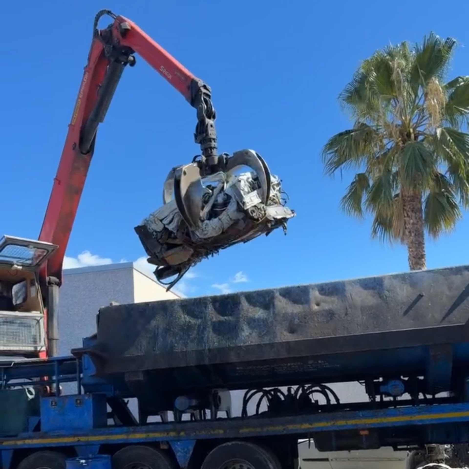 Sous un ciel bleu dégagé, le bras rouge d'une grue soulève une voiture écrasée et la dépose sur un camion plateau.
