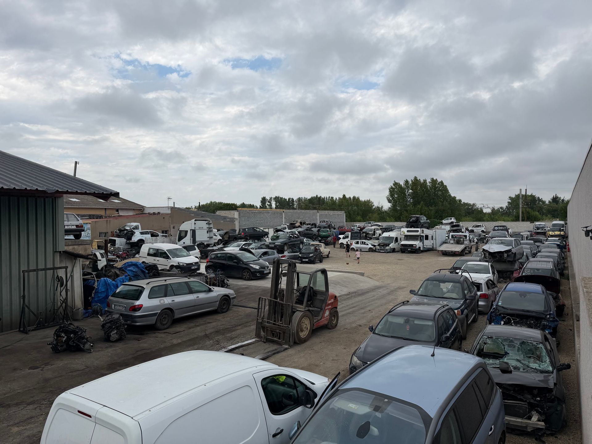 Parc à ferraille en plein air avec des rangées de voitures garées et endommagées sous un ciel nuageux.