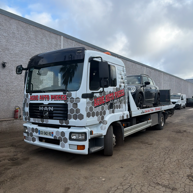 Un camion de dépannage blanc à plateau transporte une Mini Cooper noire.