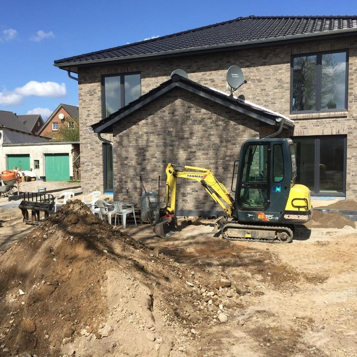 Ein gelber Bagger steht vor einem Backsteinhaus