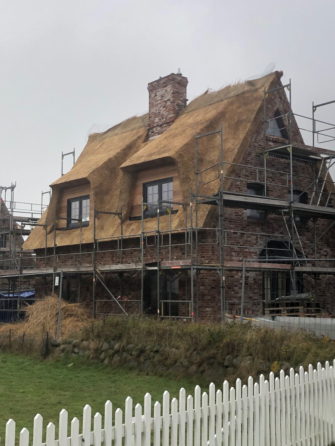 Ein Backsteinhaus mit Strohdach und Gerüst darum