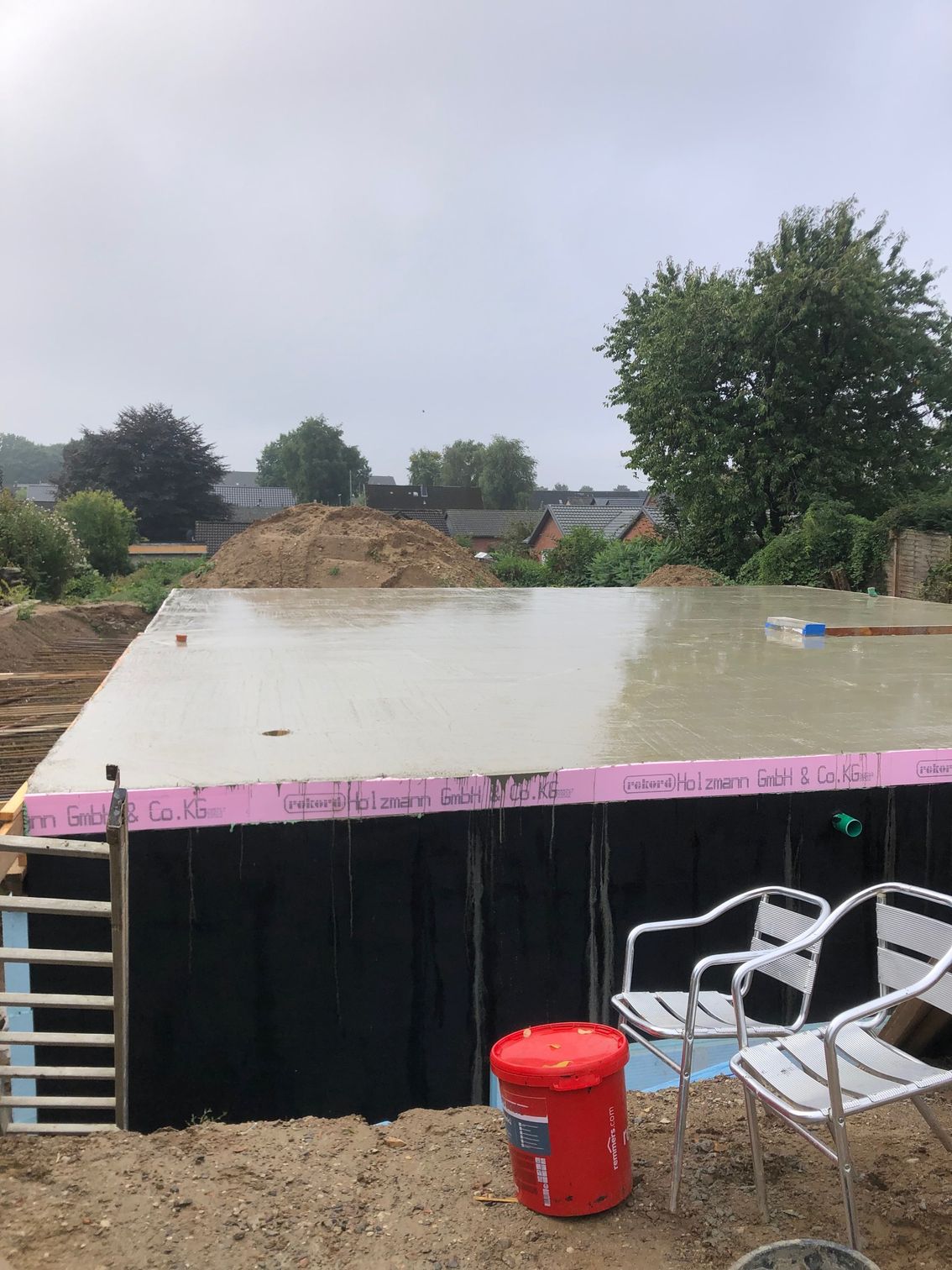 Auf einer Baustelle wird mit Stühlen und einem roten Eimer ein Betonboden gegossen.