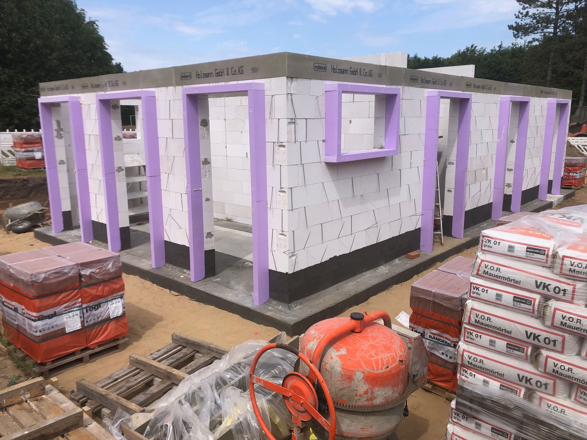 Ein im Bau befindliches Gebäude mit violetten Verzierungen und einem Betonmischer davor.