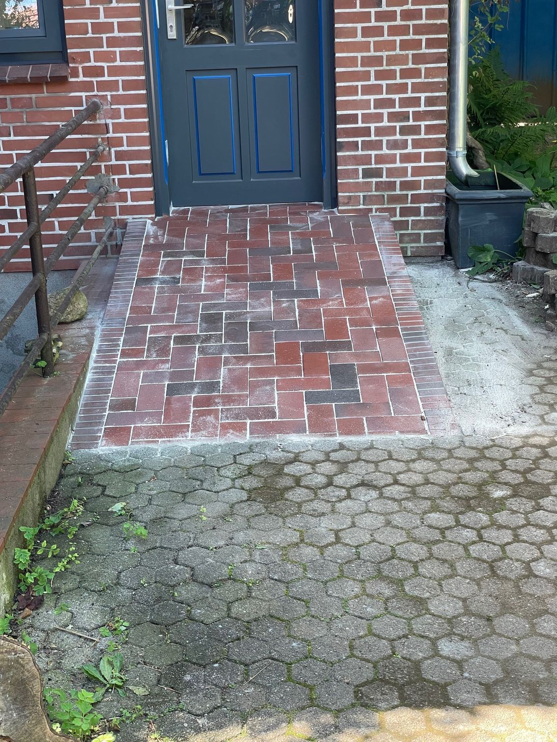 Ein gemauerter Gehweg, der zur Eingangstür eines Backsteingebäudes führt