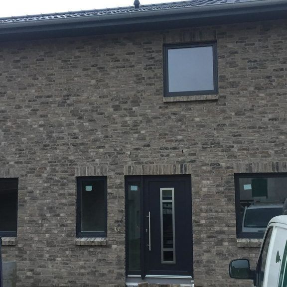 Ein Backsteingebäude mit einer schwarzen Tür und schwarzen Fenstern und einem davor geparkten Auto.