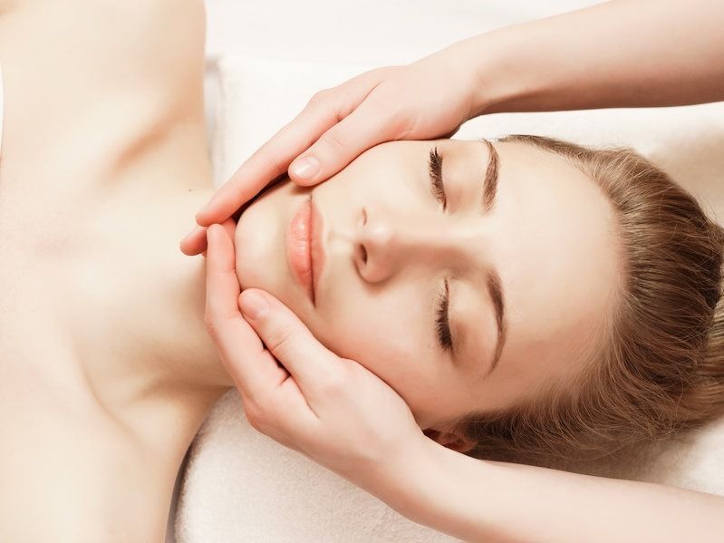 Mujer recibiendo masaje facial, manos en las mejillas, ojos cerrados, expresión serena.