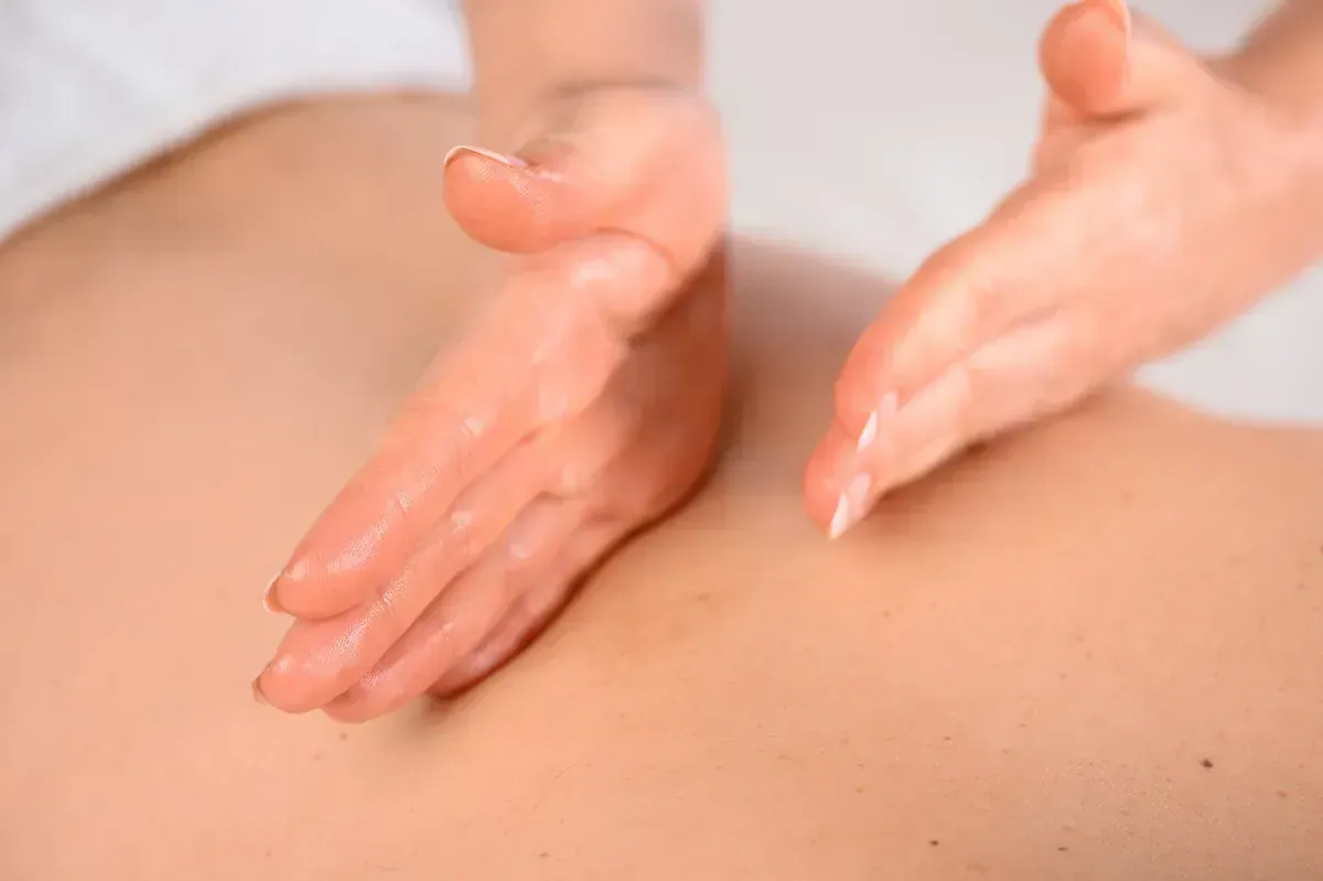 Manos dando un masaje de espalda, aplicando aceite, sobre piel pálida.