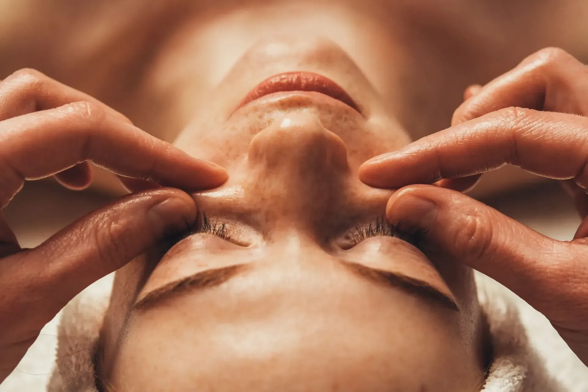 Primer plano de mujer recibiendo masaje facial, manos en la cara, ojos cerrados, expresión serena.
