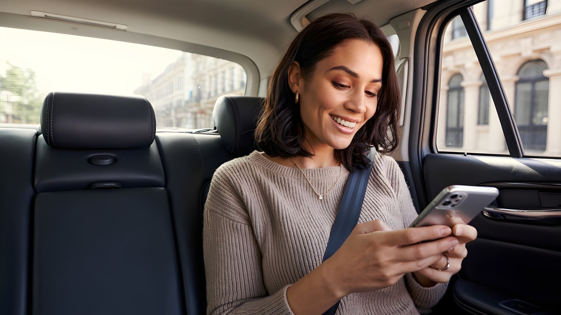 Une femme dans une voiture sourit, regarde un téléphone et porte une ceinture de sécurité.