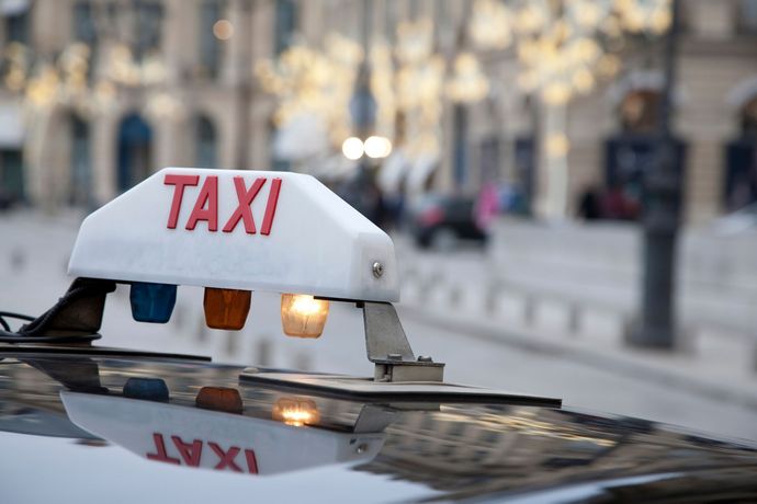 Feu de toit de taxi, blanc avec texte rouge TAXI ; lumières orange et bleues, arrière-plan flou de rue de la ville.
