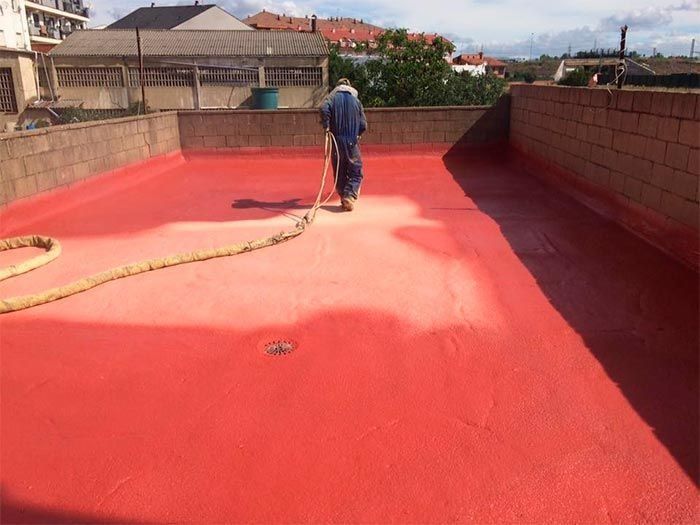 Un hombre está rociando pintura roja sobre un techo.