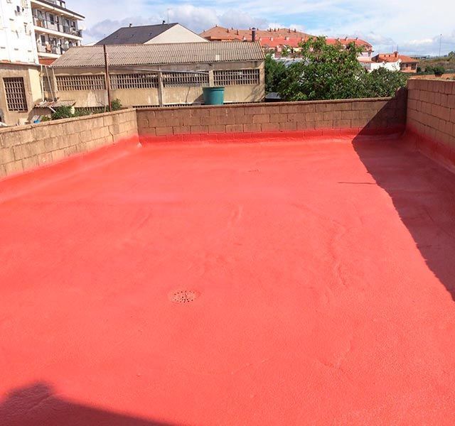 Un techo rojo con una pared de ladrillos y edificios al fondo.