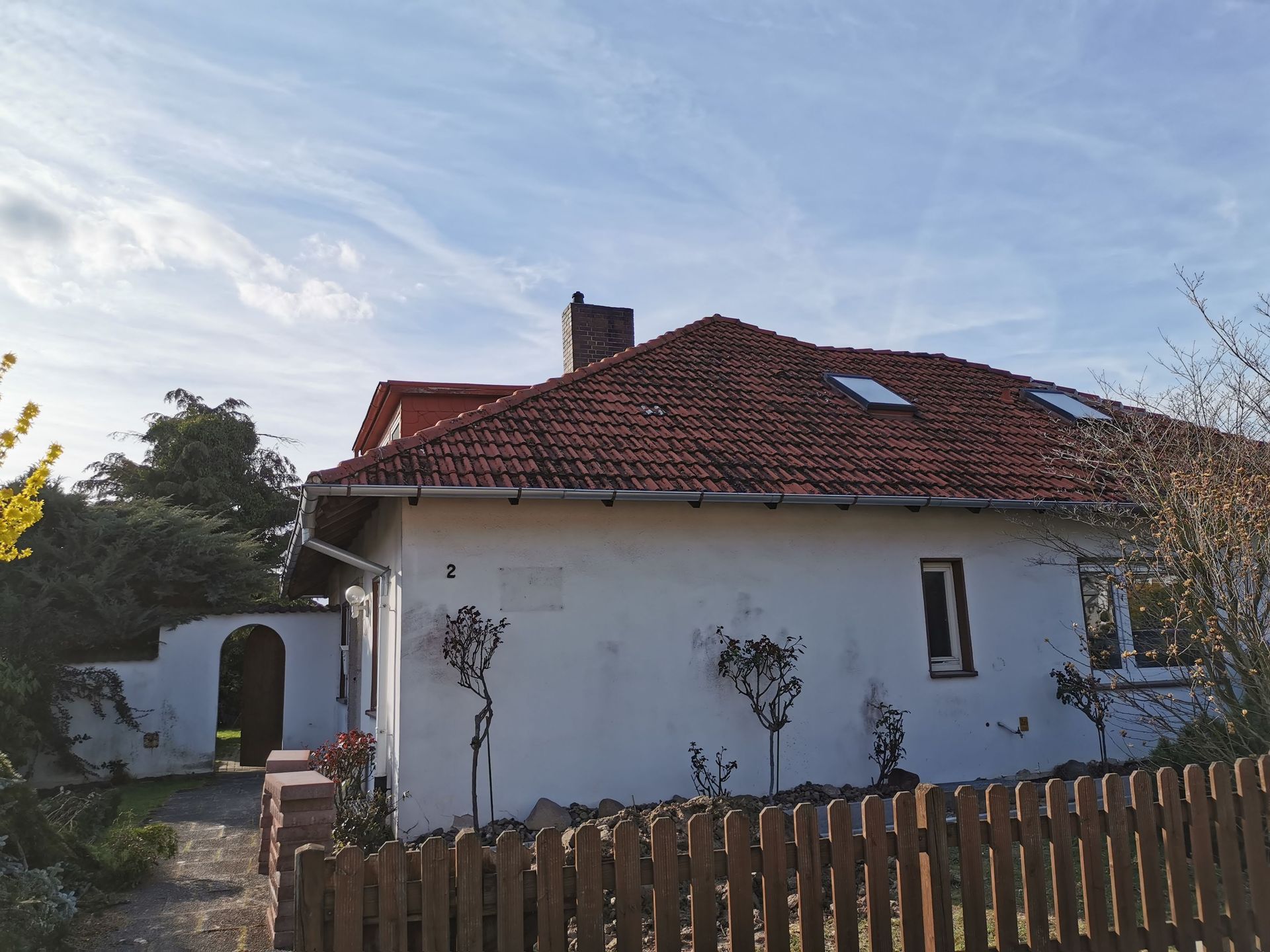 Hinter einem Holzzaun steht ein weißes Haus mit rotem Ziegeldach