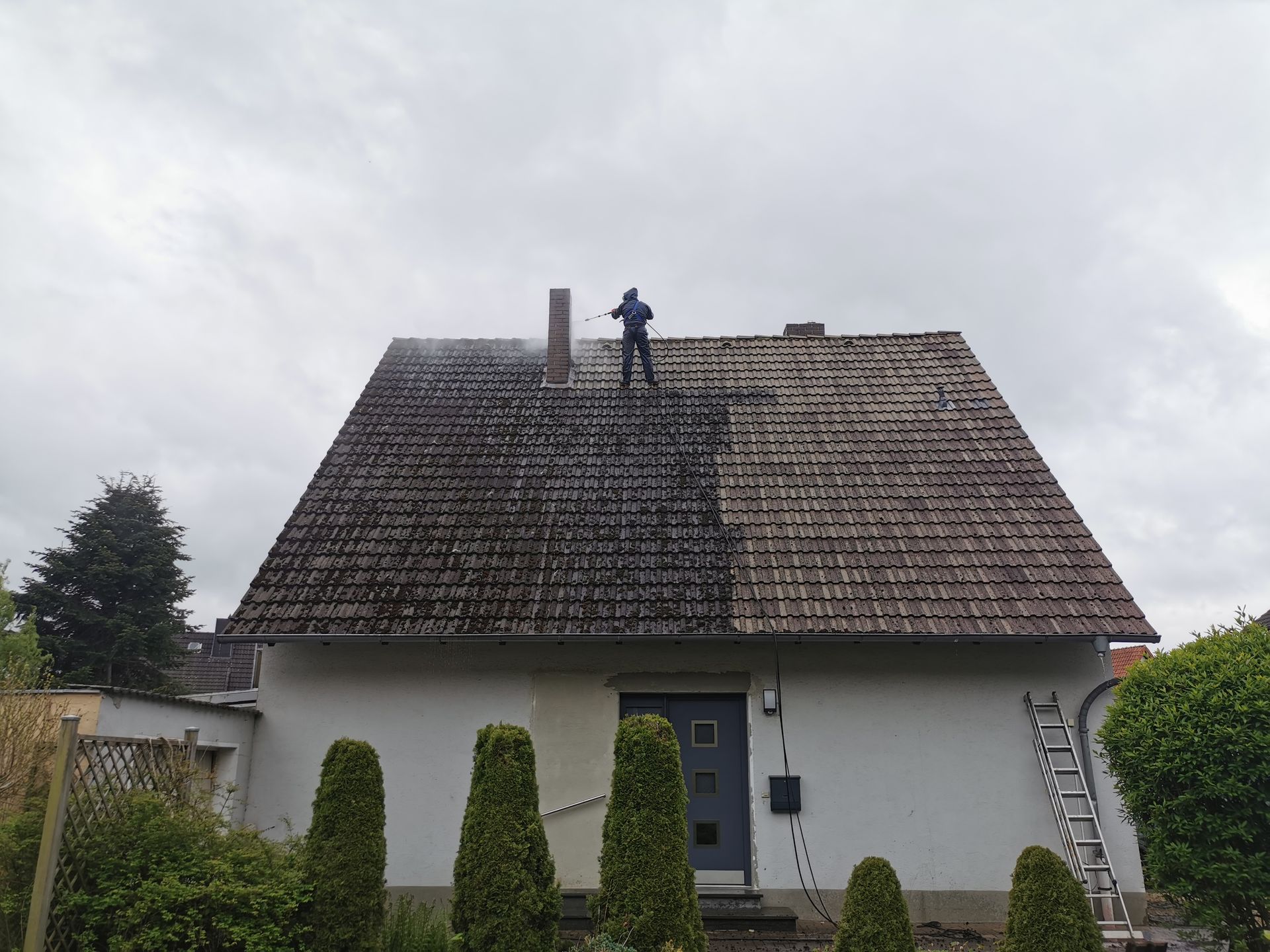 Ein Mann reinigt das Dach eines Hauses mit einem Hochdruckreiniger.
