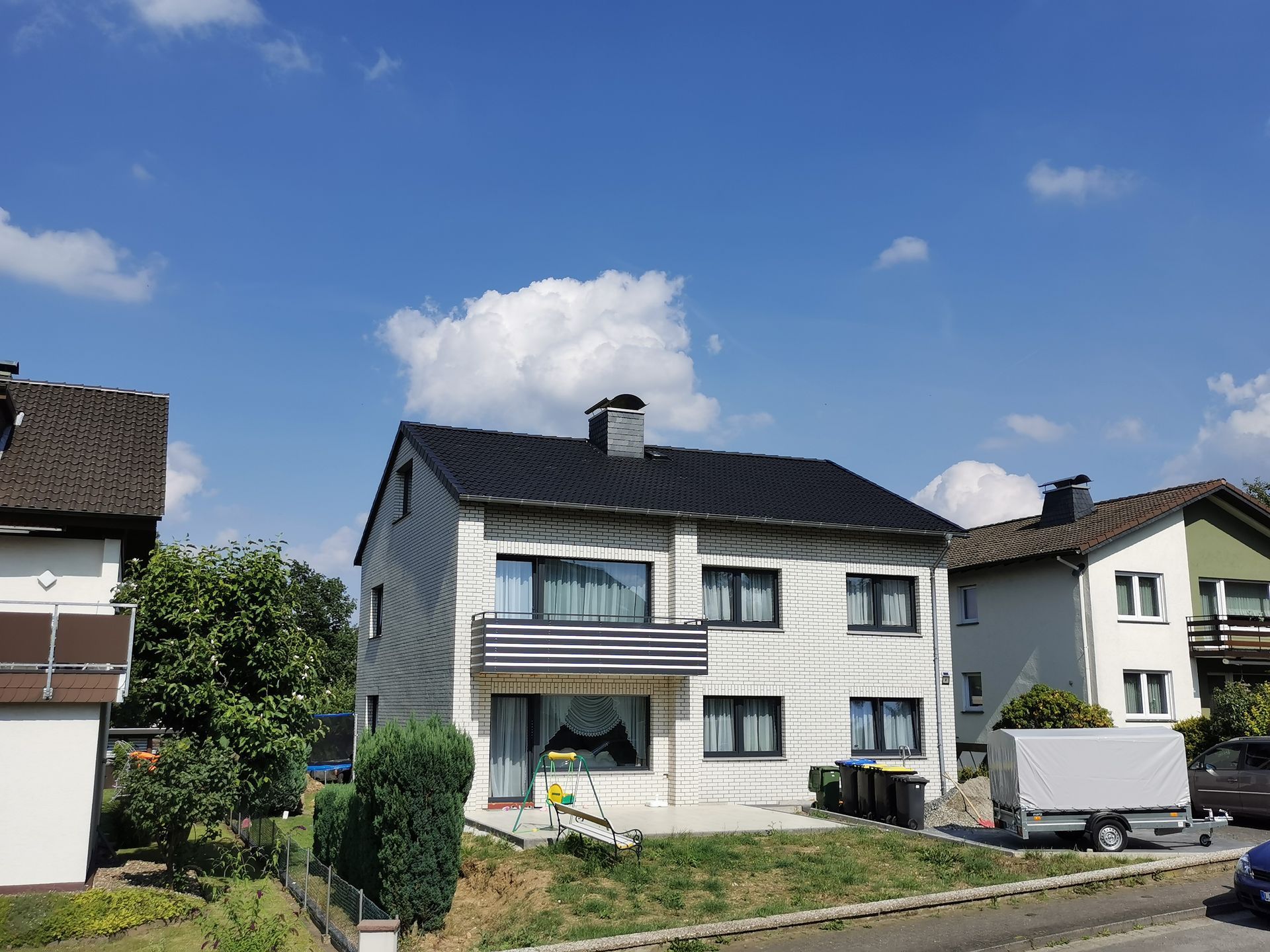 An einem sonnigen Tag ist ein weißes Haus mit schwarzem Dach von anderen Häusern umgeben.