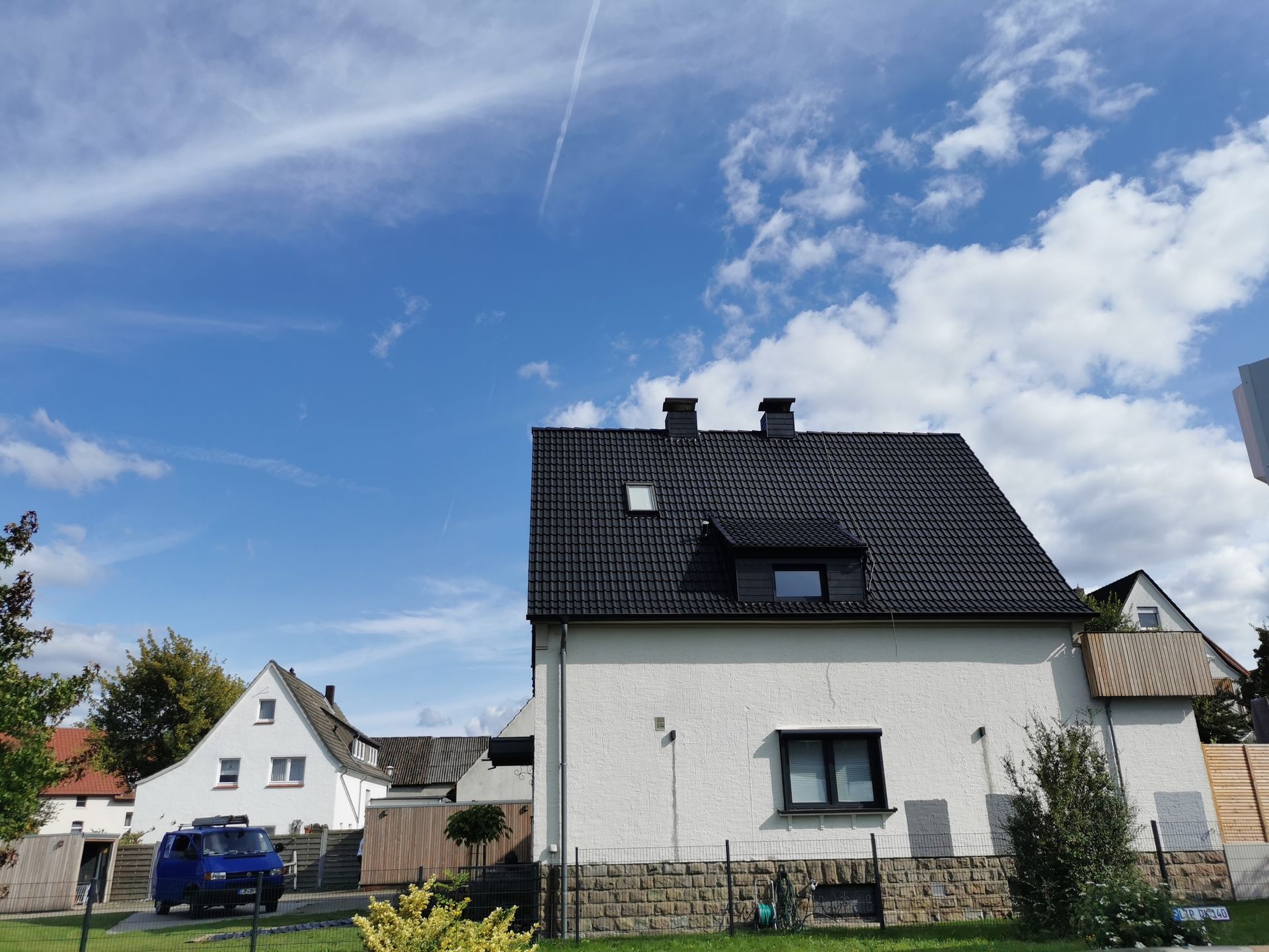 Ein weißes Haus mit einem schwarzen Dach und einem davor geparkten blauen Lieferwagen.