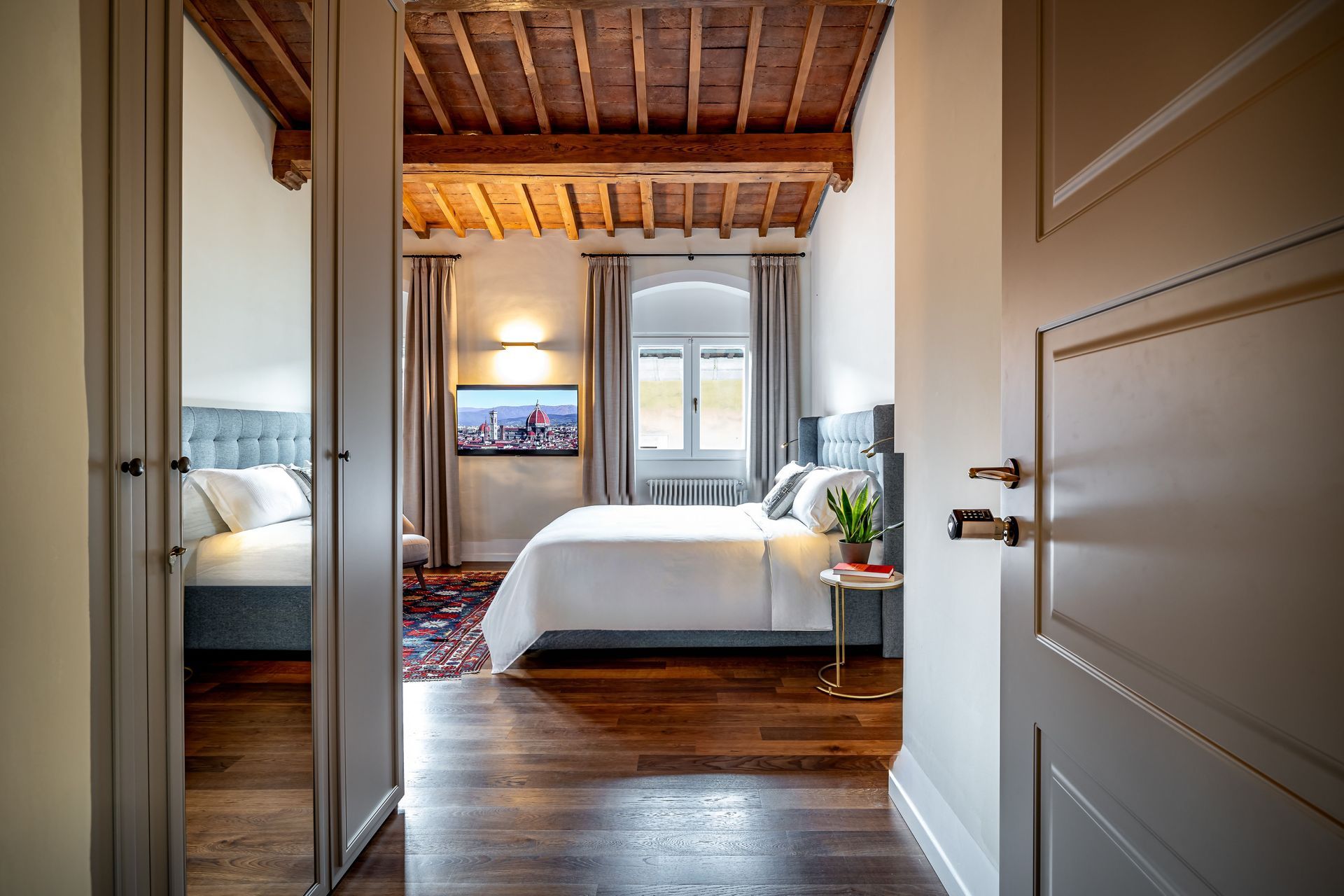 Le Torri by Dimora Collection: Hallway view into a bright bedroom with wood floors, and a bed by the window.