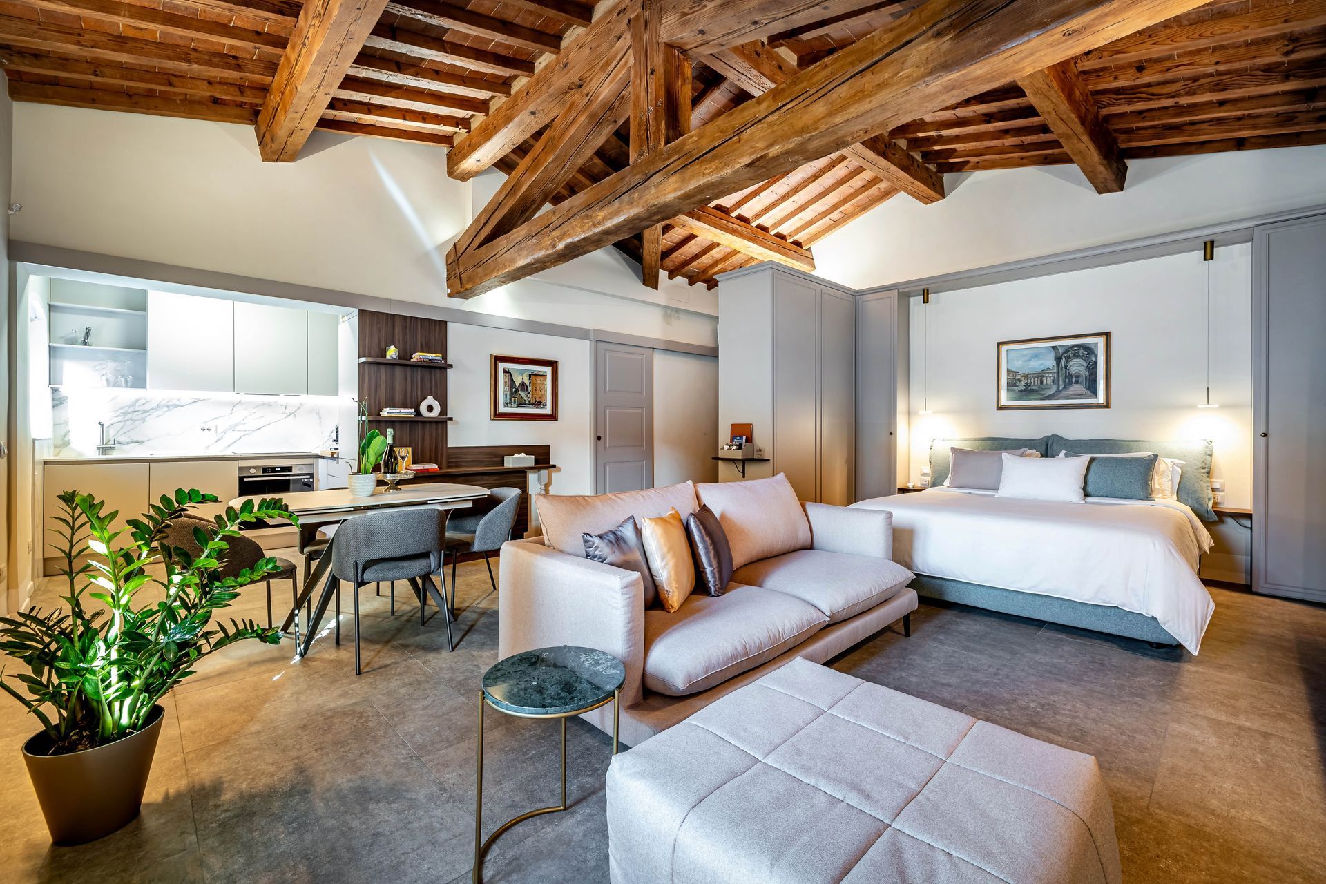 Le Torri by Dimora Collection: Cozy loft-style bedroom with exposed wood beams, dining nook, and plants in warm neutral tones