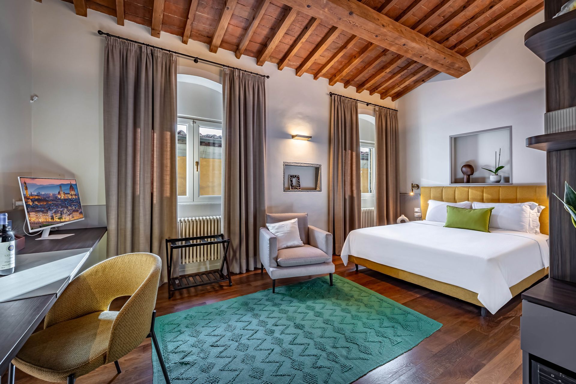 Le Torri by Dimora Collection: Modern bedroom with green rug, wooden beams, and a wine bottle on a table in the foreground
